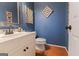 Stylish powder room featuring blue walls, hardwood floors, decorative art, and a white vanity at 245 Longshore Way, Fayetteville, GA 30215
