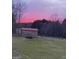 Scenic view of the backyard at dusk, featuring a storage shed and tree line against the colorful sky at 623 Swan Lake Rd, Stockbridge, GA 30281