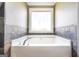 White soaking tub beneath a window, accented by tiled walls in neutral colors at 603 Honey Creek Rd, Mcdonough, GA 30252