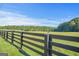 Expansive grassy pasture enclosed by a wooden fence and bordered by lush trees under a clear blue sky at 4226 Highway 155 N, Stockbridge, GA 30281