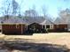 A backyard view of a red brick house with a gabled roof, mature trees, and dormant lawn at 170 Royal Ridge Way, Fayetteville, GA 30215