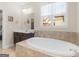 Bathroom showcasing soaking tub, tiled surround, window with blinds, and vanity in background at 109 Faversham Dr, Mcdonough, GA 30252