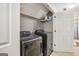 Modern laundry room with dark-colored washer and dryer, wire shelf and door to separate room at 1144 Pickets Ridge Dr, Locust Grove, GA 30248