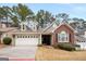 Home exterior showcases a mix of stucco and brick, dormer windows, a two-car garage, and mature trees against a blue sky at 103 Augusta Dr, Peachtree City, GA 30269