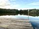 Wooden dock extending onto the calm lake with surrounding trees, reflecting a clear blue sky with clouds at 275 Old Mill Ct, Fayetteville, GA 30214