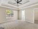 Main bedroom with a tray ceiling, neutral carpet, window, and adjacent bathroom and closet at 124 Williams Blf, Mcdonough, GA 30252