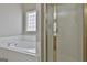 A bathtub with a small window and tiled surround next to a shower stall with a gold frame at 12241 Crestwood Ct, Fayetteville, GA 30215