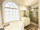 Bright bathroom with a soaking tub, glass shower, and large arched window at 345 Gaelic Way, Tyrone, GA 30290