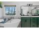 Spa-like bathroom featuring soaking tub, modern fixtures, green vanity and marble floors near a bright window at 305 Worthing Lane, Mcdonough, GA 30253