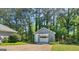 A detached garage with white trim sits in a serene, wooded setting, complemented by colorful flower beds at 230 Acorn Ct, Mcdonough, GA 30253