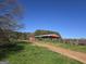 Large red barn with a metal roof and open sides, adjacent to a green field and tractor at 1761 Reavesville Rd, Bowdon, GA 30108
