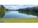 Serene lake view with calm water, lush greenery, and a grassy shoreline under a clear blue sky at 1190 Plantation Dr, Villa Rica, GA 30180