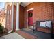 Inviting front porch with a cozy bench, decorative pillows, brick flooring, a vibrant wreath and a red brick wall at 106 Victoria Way, Carrollton, GA 30116