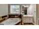 Bright bathroom featuring stone accents, a soaking tub, and decorative glass window at 4852 Jacobs Cove Pt, Buford, GA 30519