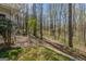 A wooded backyard with a white stone walkway along the edge of the lawn, near the siding of the house at 65 Dundee Pl, Sharpsburg, GA 30277