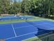 Multiple blue tennis courts with nets and lighting surrounded by trees at 9340 Basswood Way, Jonesboro, GA 30236
