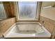 Bright bathroom featuring a white bathtub under a window, complemented by neutral tile and modern fixtures at 117 Berkeley Way, Hampton, GA 30228