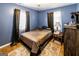 A cozy bedroom featuring hardwood floors, blue walls, a bed with warm comforter, and a small side table at 689 Hardin Rd, Temple, GA 30179