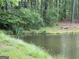 Still pond surrounded by lush vegetation and trees, with stone bench in the distance at 191 Tumlin Creek Rd # 1, Roopville, GA 30170