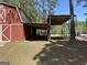 A red barn is showcased, attached to an open-air carport on a partially mowed lawn, offering ample parking and storage at 183 Busbin Rd, Fayetteville, GA 30215