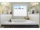 A luxurious bath tub placed between dual vanities with large mirrors and bright lighting at 2351 Rabbit Farm Cir, Loganville, GA 30052