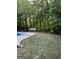 Serene backyard featuring a sparkling pool, lush lawn, and a charming greenhouse surrounded by mature trees at 135 Danube Trl, Stockbridge, GA 30281