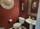 Stylish powder room with dark red walls, unique mirror, silver wall decorations, and pedestal sink at 1007 Oglethorpe Ct, Woodstock, GA 30188