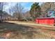 Backyard showing a red storage shed and large trees, with a mix of grass and leaves on the ground at 113 Elmwood Dr, Hampton, GA 30228