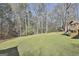 Large grassy backyard with a playset, wooded area, and a fenced in structure in the distance at 100 Rockland Trl, Sharpsburg, GA 30277