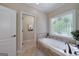 Bathroom featuring soaking tub with tiled surround, decorative window, and adjacent doorway at 330 Noah Pl, Mcdonough, GA 30252