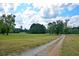 Gravel driveway winds through a grassy, open field with scattered trees under a partly cloudy sky at 301 Spruill Bridge Rd, Temple, GA 30179