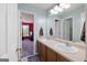 Light blue bathroom with double sinks on a wooden vanity, neutral tile floors, and an open doorway at 125 Anna Dr, Covington, GA 30014