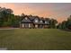 Evening shot of a two-story home with a well-manicured lawn and mature trees, highlighted by a colorful sunset sky at 189 Willowleaf Way, Sharpsburg, GA 30277