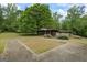 Backyard view of a one-story house with unique landscaping and a concrete parking area surrounded by trees at 5493 Alexanders Lake Sw Rd, Stockbridge, GA 30281