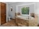 Bright bathroom with a large bathtub, beige tile and a window overlooking a wooded view at 930 Singley Dr, Locust Grove, GA 30248