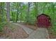Storage shed with red walls and a concrete path surrounded by leafy trees and shrubs at 120 Hermitage Pl, Peachtree City, GA 30269