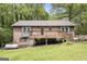 Back of brick home with a wooden deck, mature trees, landscaping, and a propane tank at 165 White Rose Ln, Temple, GA 30179