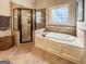 Elegant bathroom featuring a soaking tub, tiled shower, and natural light from a glass block window at 106 Tullamore Trl, Tyrone, GA 30290