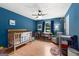 A bedroom featuring blue walls, ceiling fan, a crib, soft chair and toys at 270 Lake Cir, Fayetteville, GA 30215