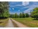 Gravel driveway through a grassy field with tree lined sides and a building in the distance at 1170 Peeksville Rd, Locust Grove, GA 30248