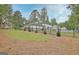 View of the house, garage, and backyard from the edge of the property line, near the wood line and pines at 400 Walnut Grove Rd, Peachtree City, GA 30269