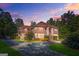 Stately brick home at dusk, featuring a circular driveway and well-manicured landscaping surrounded by mature trees at 7523 Kimberly Lynn Ct, Lithonia, GA 30058