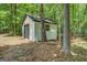 White outbuilding featuring a roll-up door and a window nestled amongst trees at 857 Cooper Rd, Social Circle, GA 30025