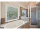 Bathtub with a tile surround and a glass-enclosed shower in a sun-filled bathroom at 1979 Alcovy Shoals Blf, Lawrenceville, GA 30045