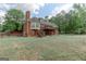 Expansive backyard showcasing a brick home with a wooden deck and lush green trees, offering a serene outdoor living space at 135 Magnolia Dr, Oxford, GA 30054