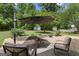 Stone patio featuring cushioned seating, a table, an umbrella, a fire pit, and a view of two storage sheds in the backyard at 115 Roscommon Ct, Tyrone, GA 30290
