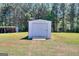 A white storage shed with a roll-up door sits on a lawn in a wooded area at 1621 Dixie Rd, Covington, GA 30014