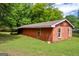 Side view of a red wooden storage shed with a covered area and green grass at 74 Price W Dr, Locust Grove, GA 30248