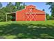 Quaint red barn with white trim surrounded by a green grass and mature trees, adding rustic charm to the landscape at 228 Indian Creek Rd, Locust Grove, GA 30248