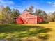Spacious red barn with a classic white trim and sliding doors, set in a beautiful green meadow under a clear sky at 228 Indian Creek Rd, Locust Grove, GA 30248